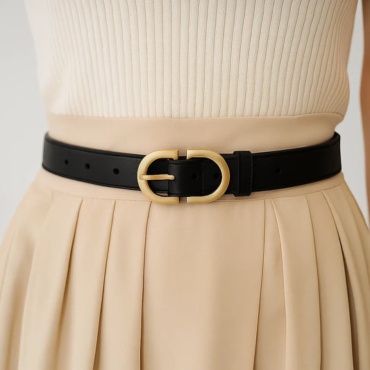 cinturón negro de cuero sintético con hebilla ovalada dorada visto frontalmente sobre falda clara