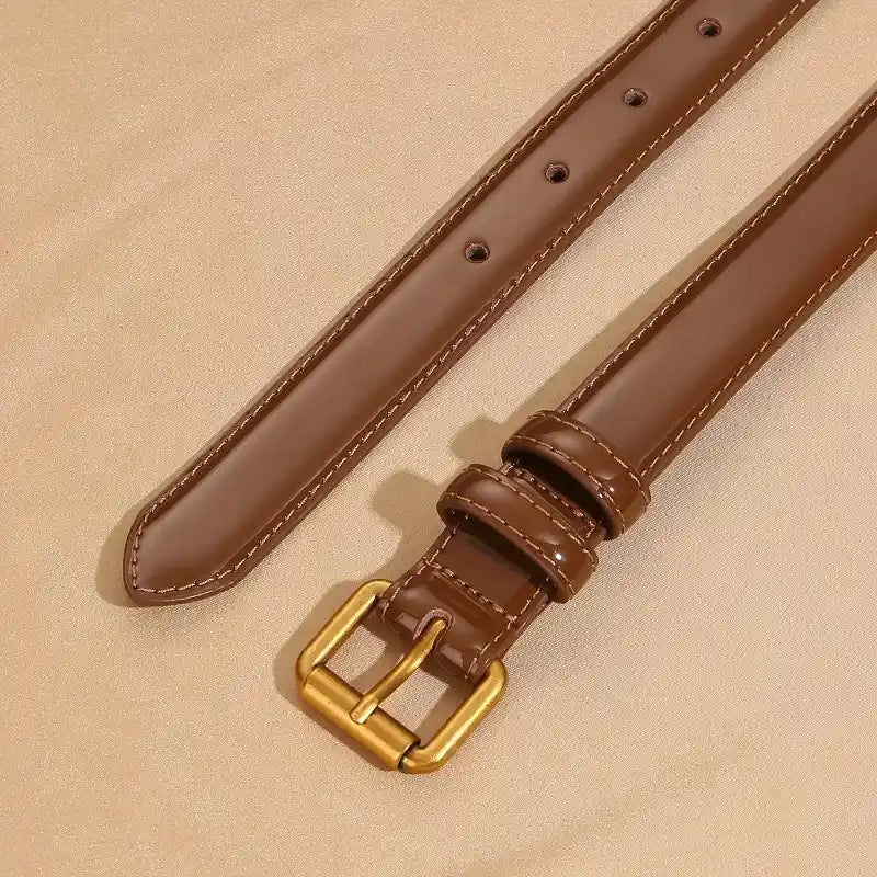 vista superior de cinturón marrón de charol con hebilla dorada sobre fondo beige